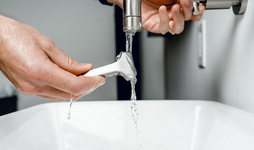 Man cleaning razor blade in sink faucet